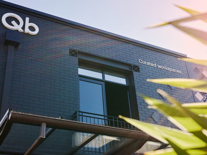 Dark brick building facade with Qb logo and curated workspaces text, viewed from below