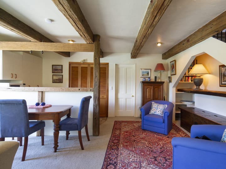 Cottage interior with exposed timber beams, a dining table and sitting area looking to the garden