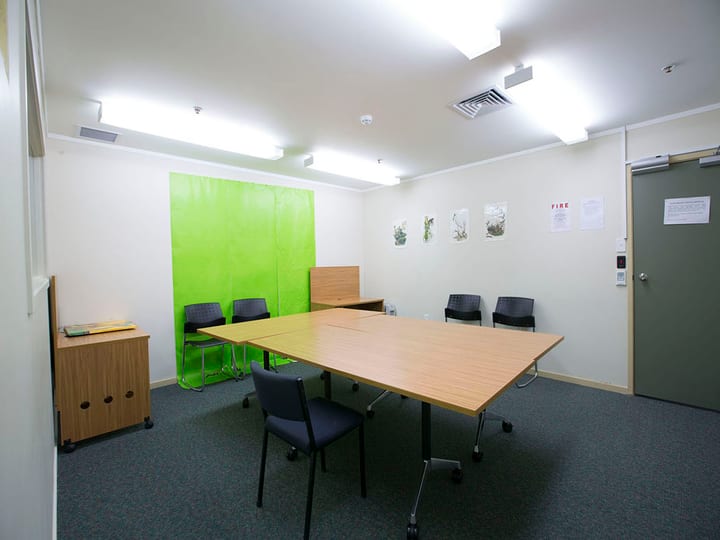 Small meeting room with timber tables, chairs, green feature wall, and artworks