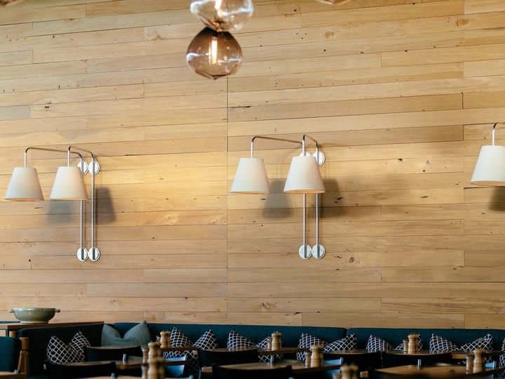 Restaurant wall with timber cladding and wall-mounted lamps above banquette seating