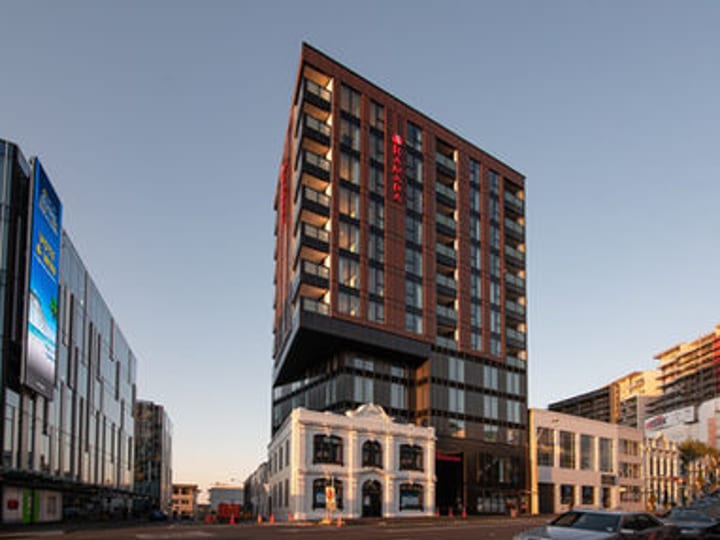 Tall hotel building with dark and terracotta cladding at dusk on a city street