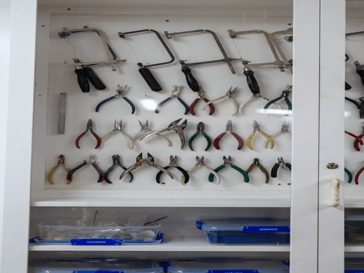 Cabinet open to show rows of pliers, saws and craft tools on a board