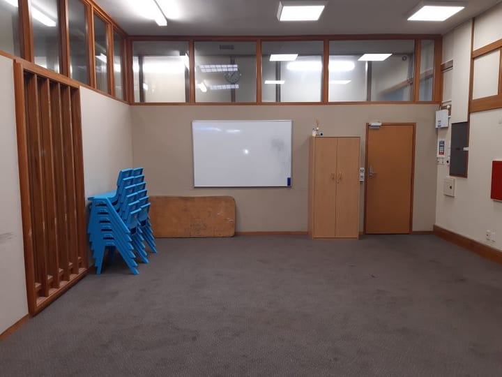 Empty carpeted room with stacked blue chairs, whiteboard and high windows