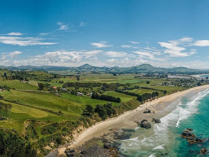 Aerial panorama of sandy beach, turquoise water and green farmland stretching to distant hills