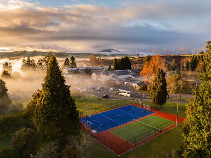 Aerial view of resort grounds with sports courts, trees, and misty hills beyond