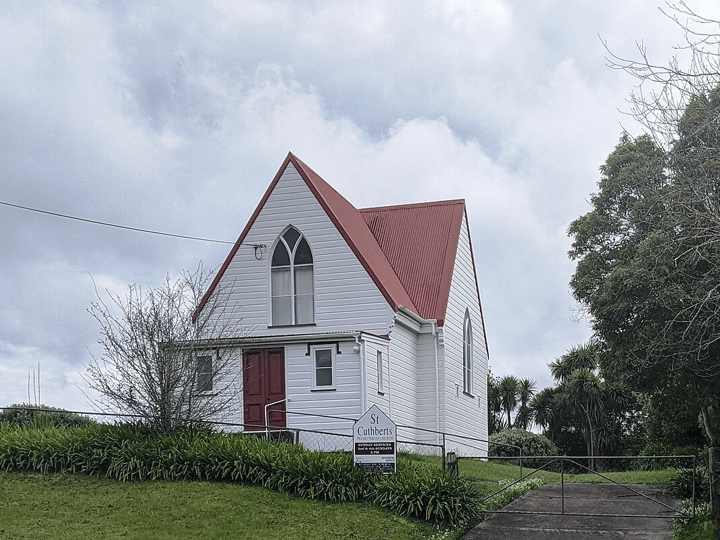 White timber church building with red corrugated iron roof and gothic arched window