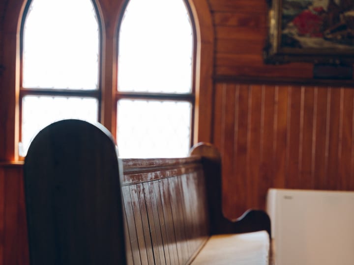 Timber church pews with gothic arched windows in background and panelled walls