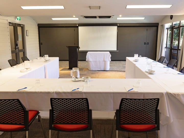 Conference room with white tablecloth U-shape layout, red-seated chairs, partition wall, and projection screen