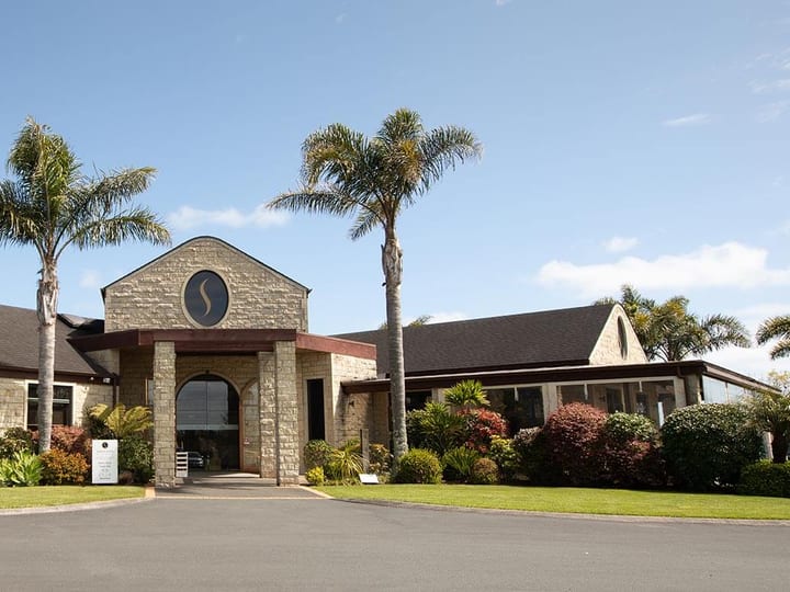 Stone and timber winery building with palm trees and formal driveway