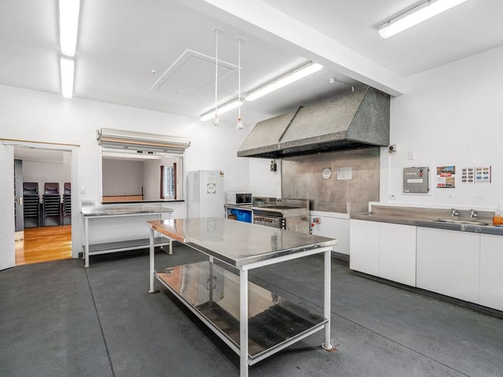 Commercial kitchen with stainless steel benches, large extraction hood, and white walls