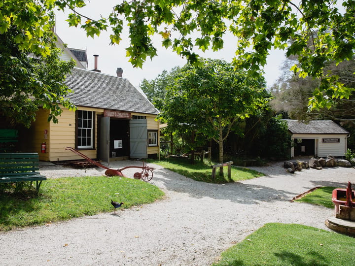 19th-century village buildings amid trees with gravel paths and farm equipment