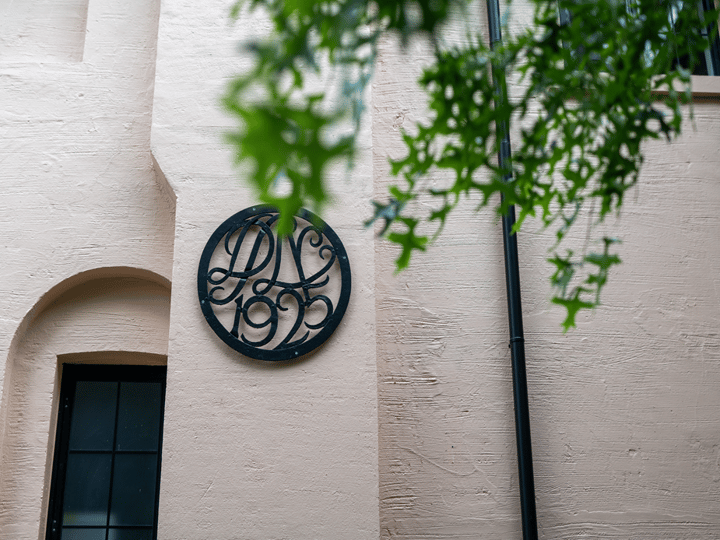 Circular wrought-iron date plaque on a render wall with overhanging tree foliage