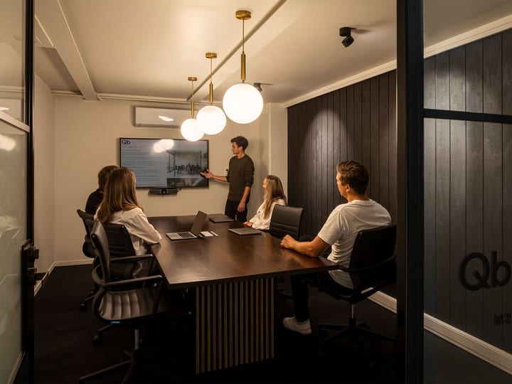 Dark-toned meeting room with timber boardroom table, globe pendants, and dark slatted wall panel