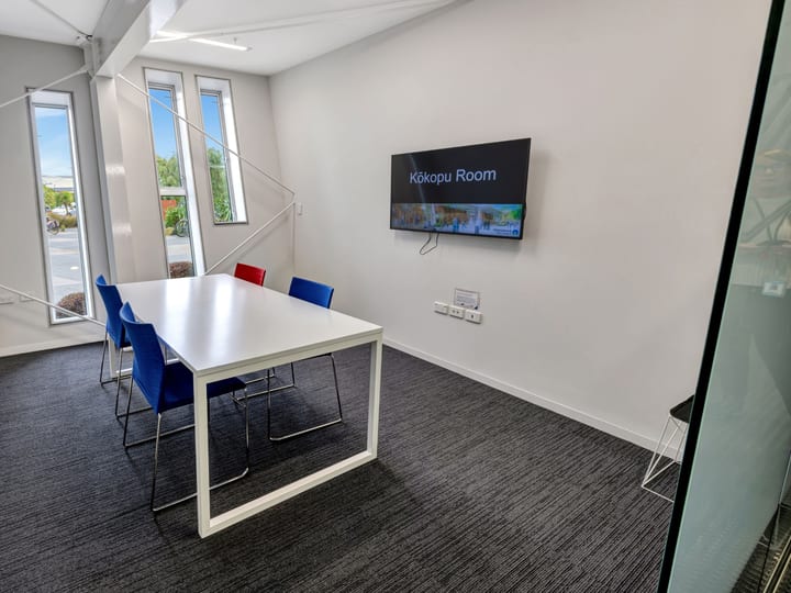 Small meeting room with white table and coloured chairs, glazed walls