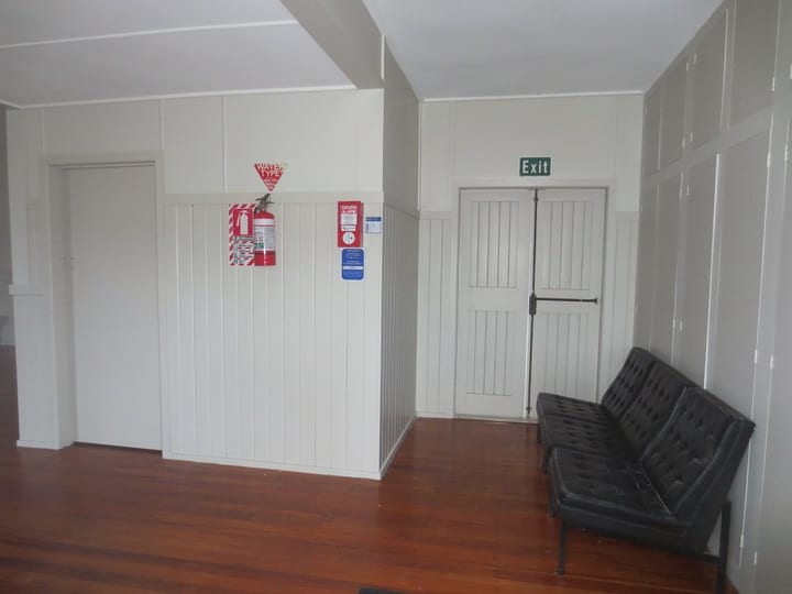 Plain white hall foyer with white panelled walls, timber floor, and black bench seat