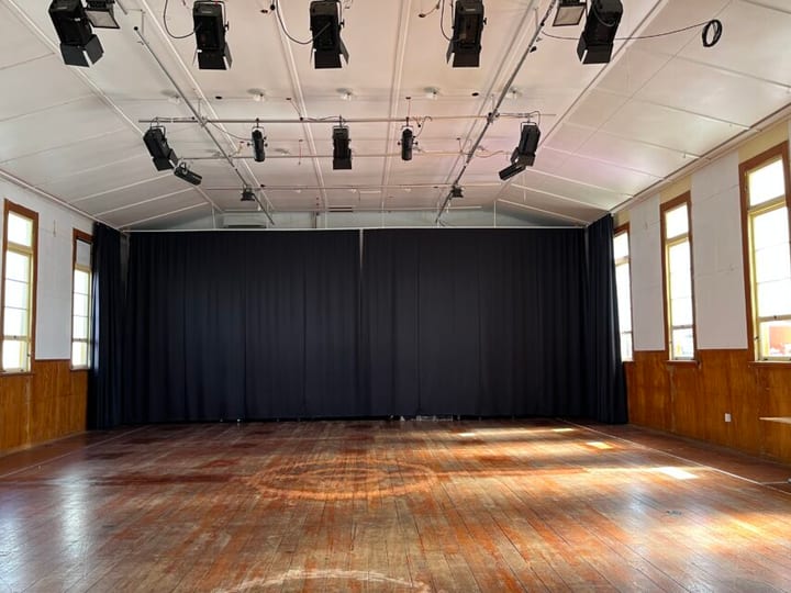 Heritage hall interior with timber floor, stage drapes, and stage lighting rig