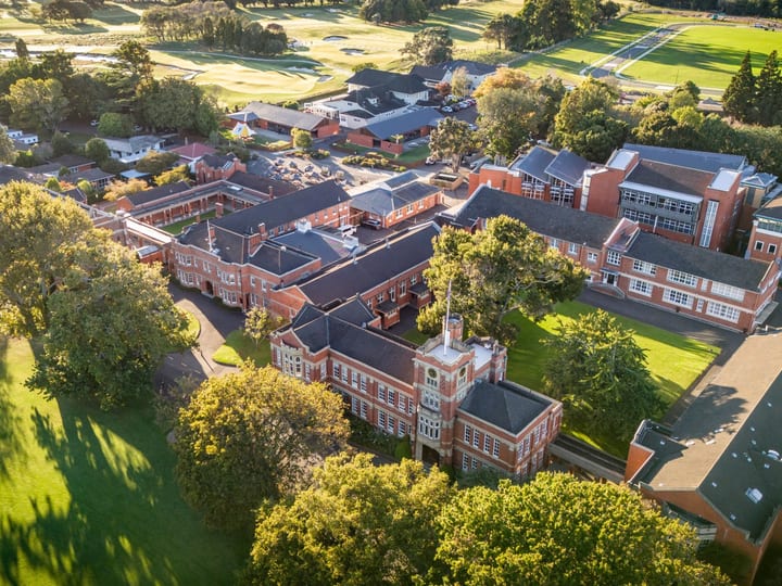 Aerial view of red brick campus buildings surrounded by trees and sports fields