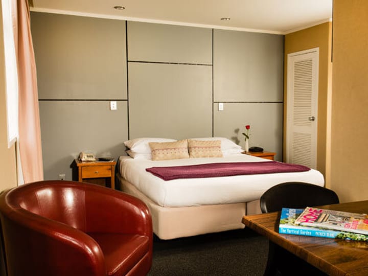 Hotel room with upholstered bed, armchair and timber side table