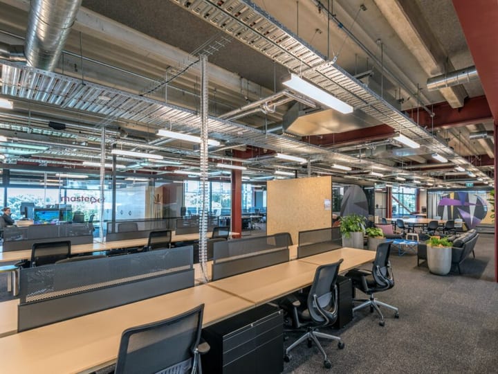 Open-plan co-working space with bench desks, exposed ducting, and red structural columns