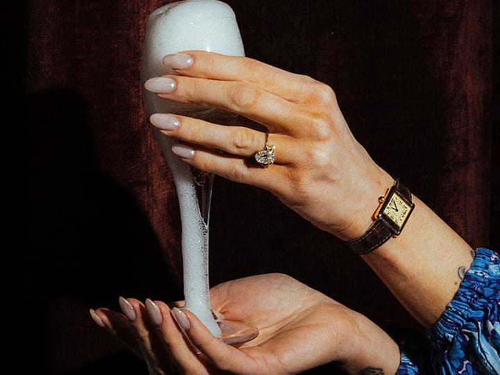 Close-up of hands holding a foaming champagne flute with a ring visible
