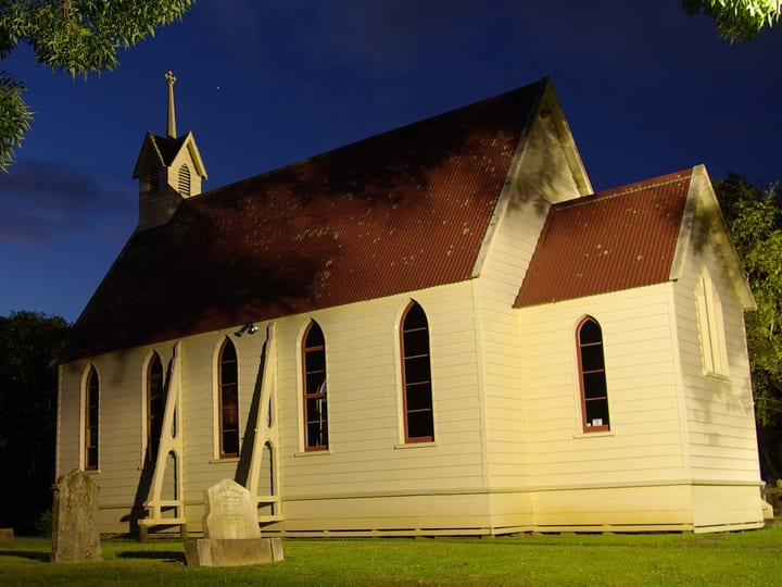 Small white timber church illuminated at night with historic graves in foreground