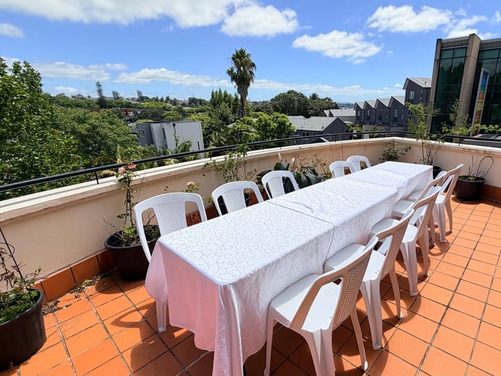 Rooftop terrace with long white-clothed table, white chairs, and city views in background