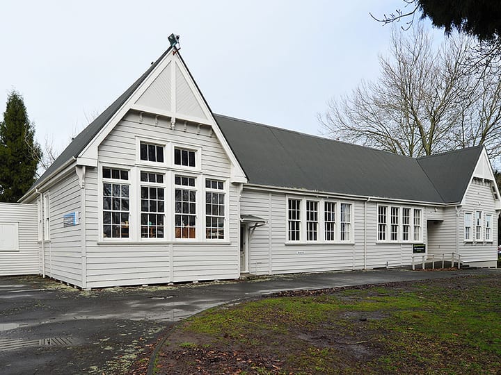 White weatherboard hall exterior from driveway angle with trees