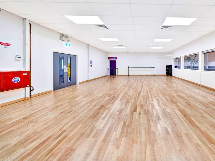 Open timber-floored hall with white walls, windows onto adjacent gym and coloured exit doors