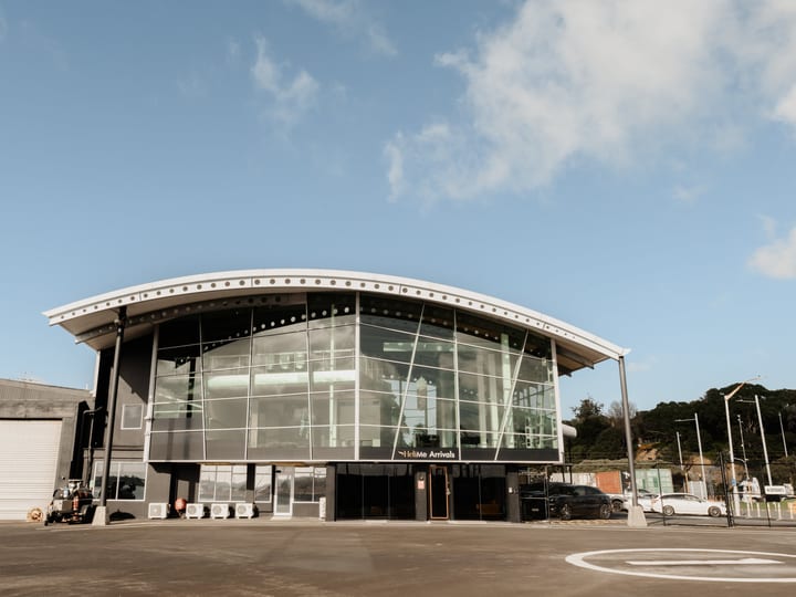 Curved glass and steel waterfront building with helipad markings in foreground