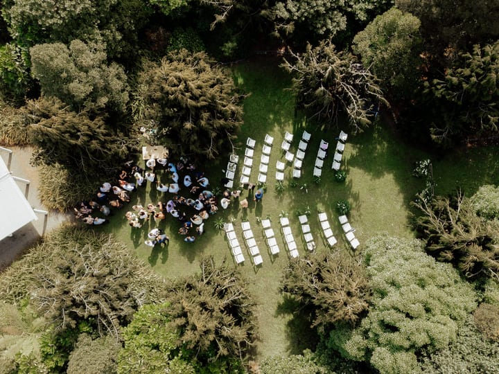 Aerial view of outdoor ceremony with white chairs set in rows and guests gathered on lawn