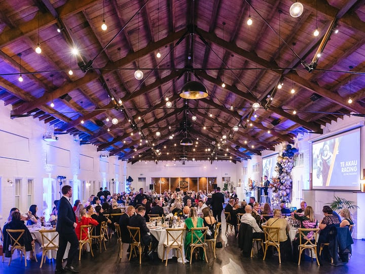Large heritage hall with timber ceiling, festoon lights, and round tables set for dining