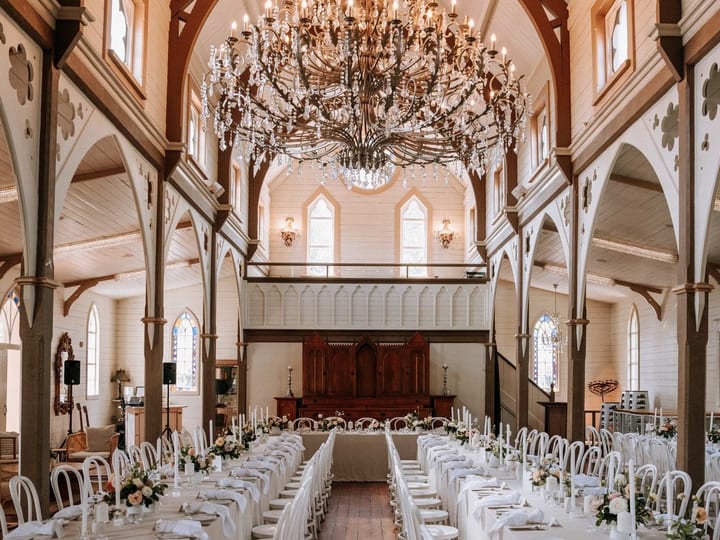White timber church interior with arched nave, large chandelier and long tables set for dining
