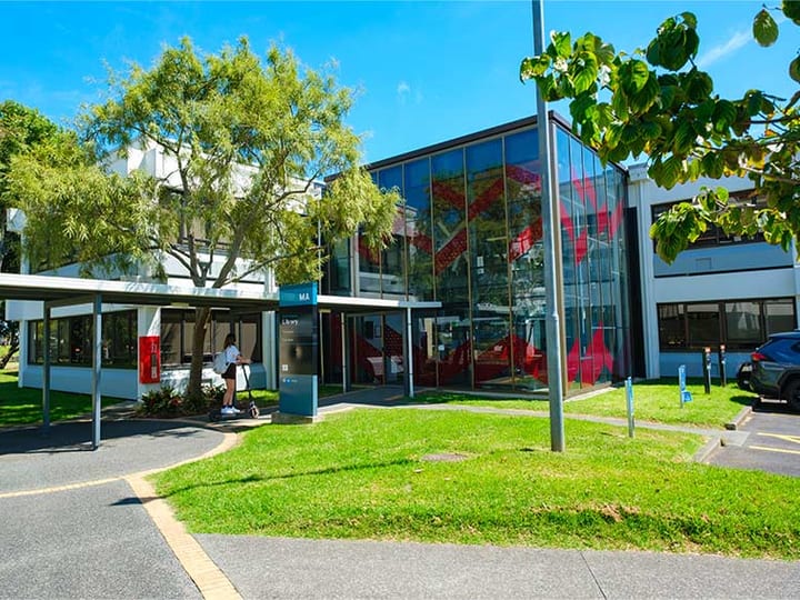 Campus building exterior with glass facade, lawn, and trees under a blue sky