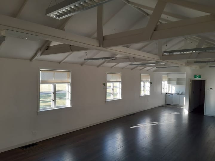 Empty hall with exposed timber trusses, floor-to-ceiling windows and dark timber floor