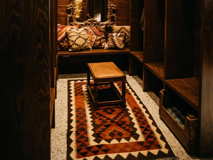 Dark timber-panelled lounge nook with a gilt mirror, kilim rug and built-in bench seating