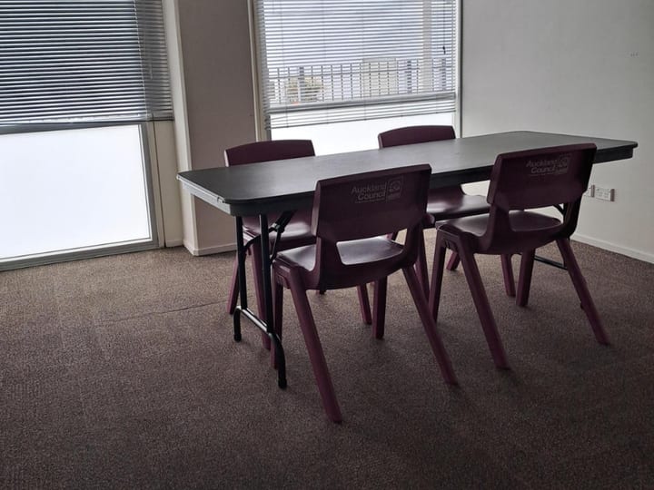 Small carpeted meeting room with dark folding table and purple chairs by window