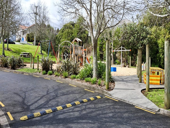 Playground with climbing structures on bark chip surface beside sealed path, trees surrounding