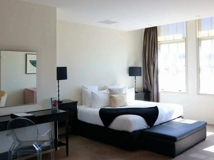 Bright hotel room with large windows, king bed, black furniture, bench seat and desk