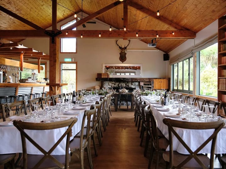 High-stud timber-framed reception hall with long banquet tables, a stone fireplace and string lights