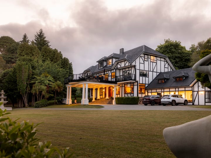 Large Tudor-style manor house with white and dark timber facade set on lawn at dusk