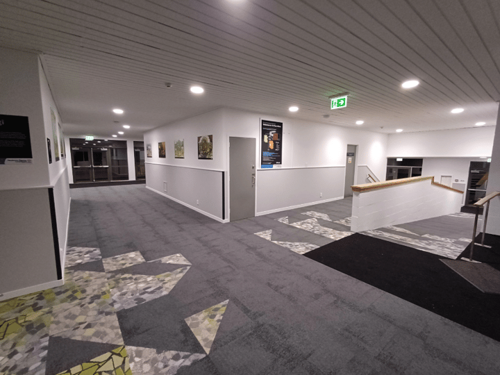 Interior corridor with patterned carpet and green geometric shapes, white walls, and recessed lighting