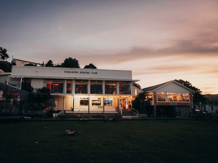 Vogelmorn Bowling Club building lit up at dusk with green lawn in foreground