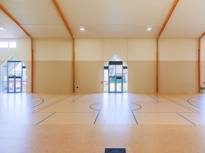Large sports hall with multi-court timber floor, high ceiling, and three sets of folding doors