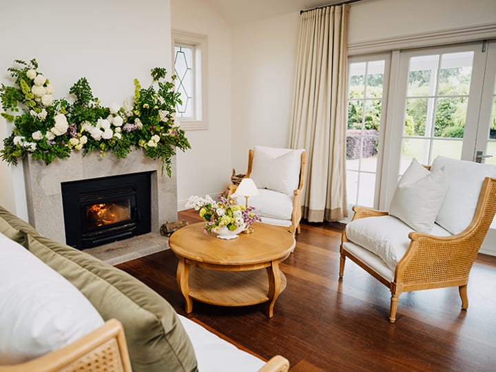 Homestead sitting room with fireplace, floral mantle arrangement, and cane armchairs