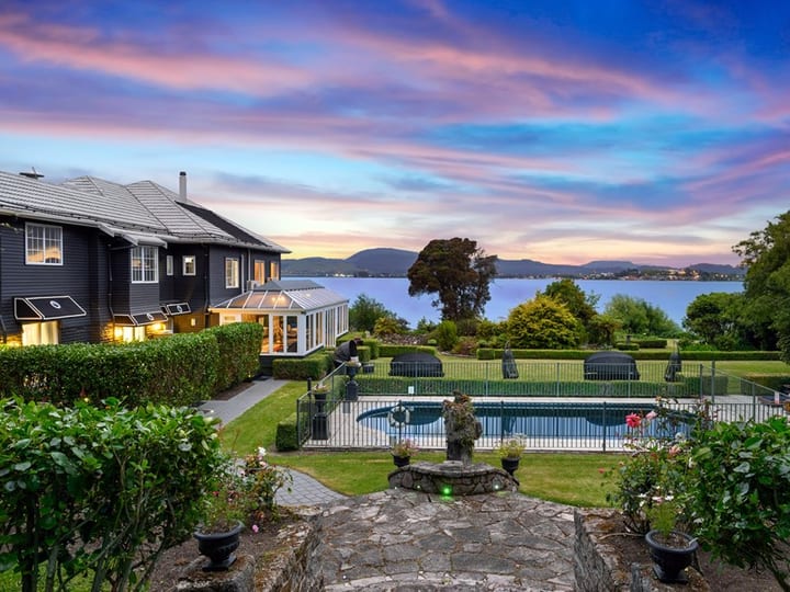 Evening view of hotel building with pool, garden, and lake at dusk
