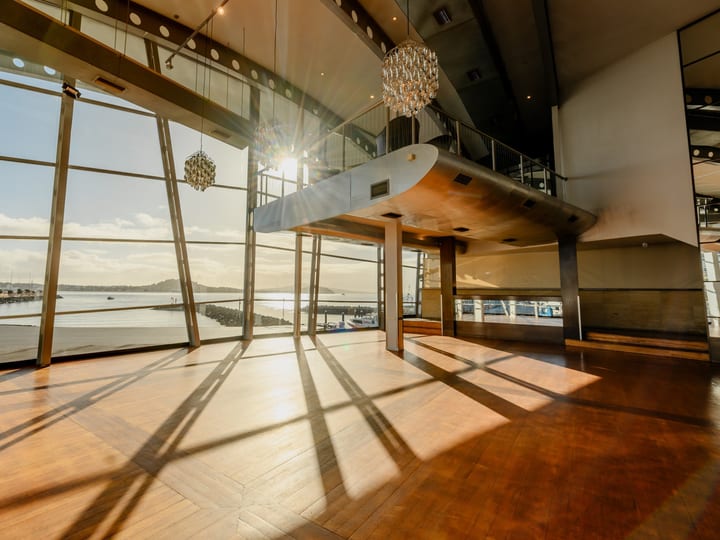 Curved steel and timber interior with large windows overlooking a waterway, suspended mezzanine and pendant lights
