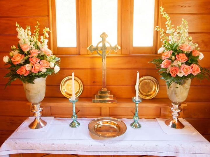 Church altar with cross, candles and flower arrangements on timber panelled walls