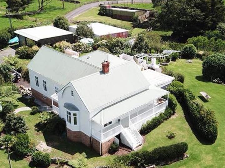 White two-storey homestead with verandah and metal roof, aerial view over green lawns