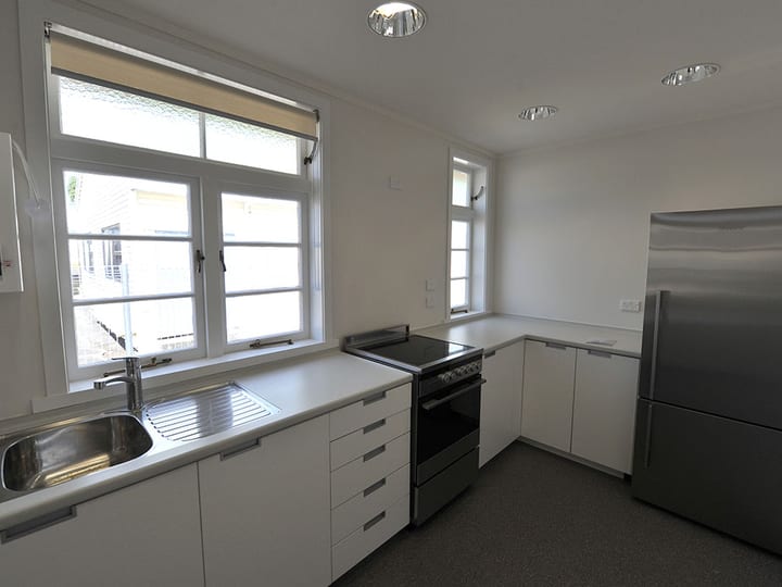 Clean white kitchen with sink, stove, refrigerator and roller blinds