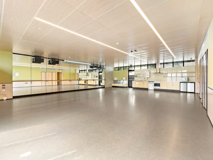 Large open room with timber-panelled ceiling, mirror wall, polished concrete floor, and fitted kitchen